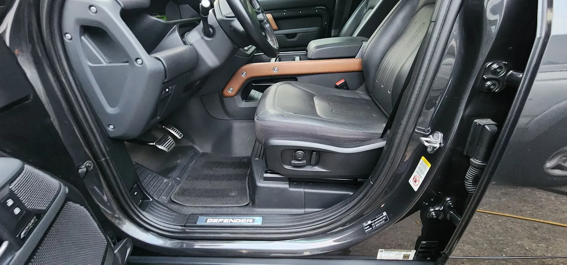 Open car door showing black leather front seat, wood trim, and illuminated door sill.
