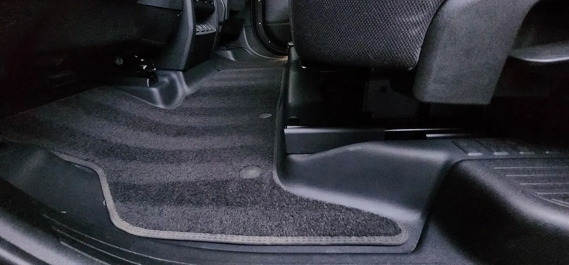 Car floor mat beneath front seat, black and gray interior upholstery.