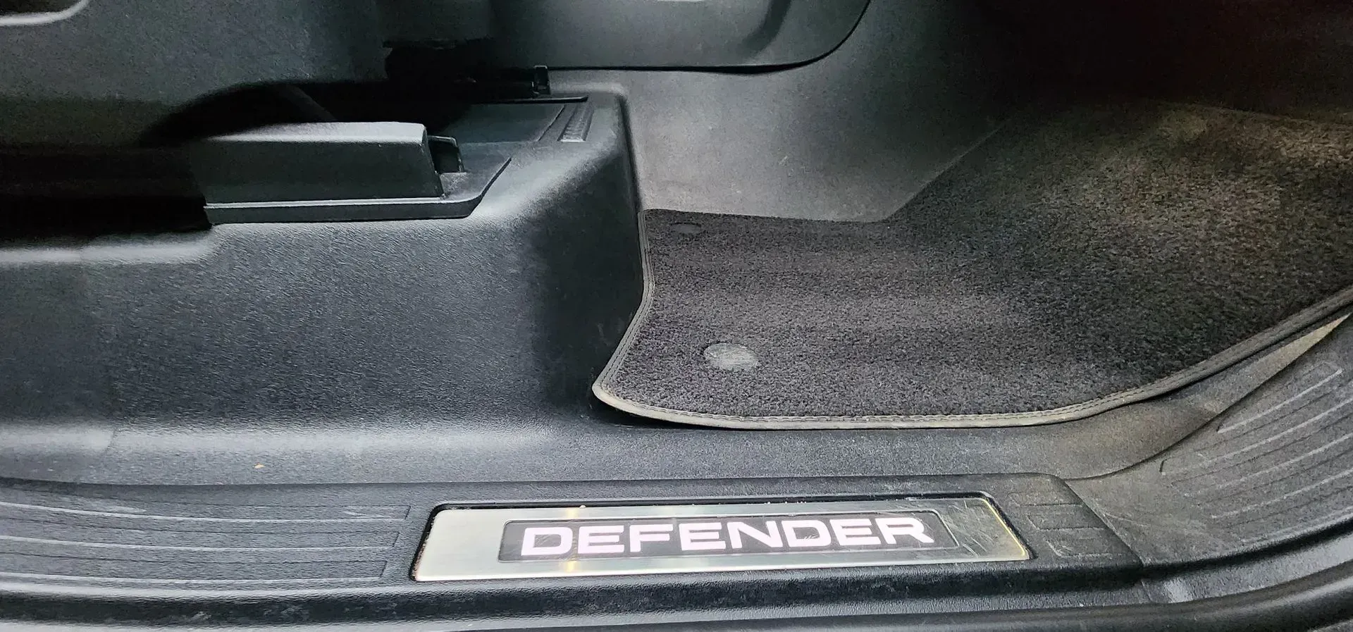 Close-up of a Land Rover Defender door sill and floor mat inside the vehicle.