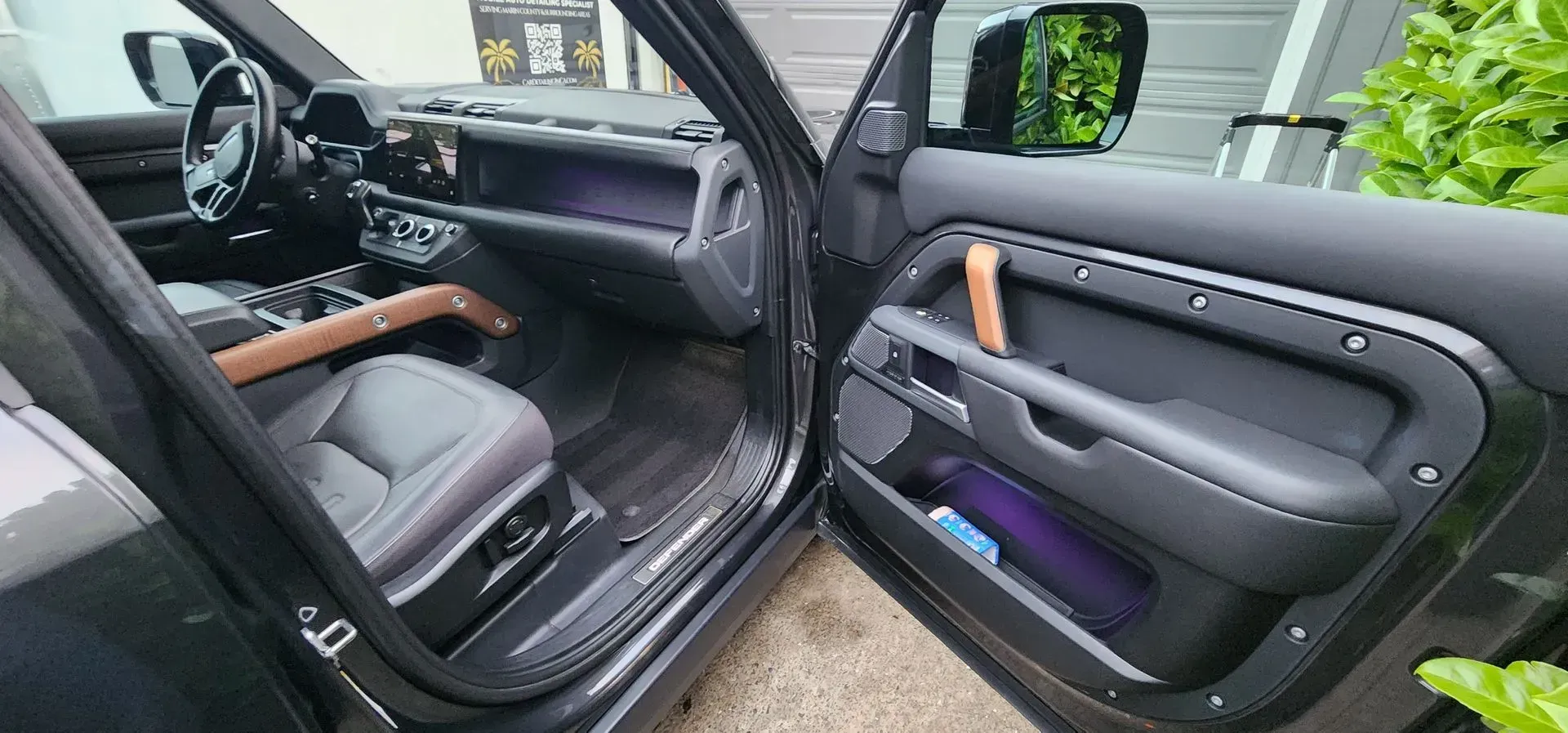 Black car interior with open rear door, showing gray seats and wood trim.