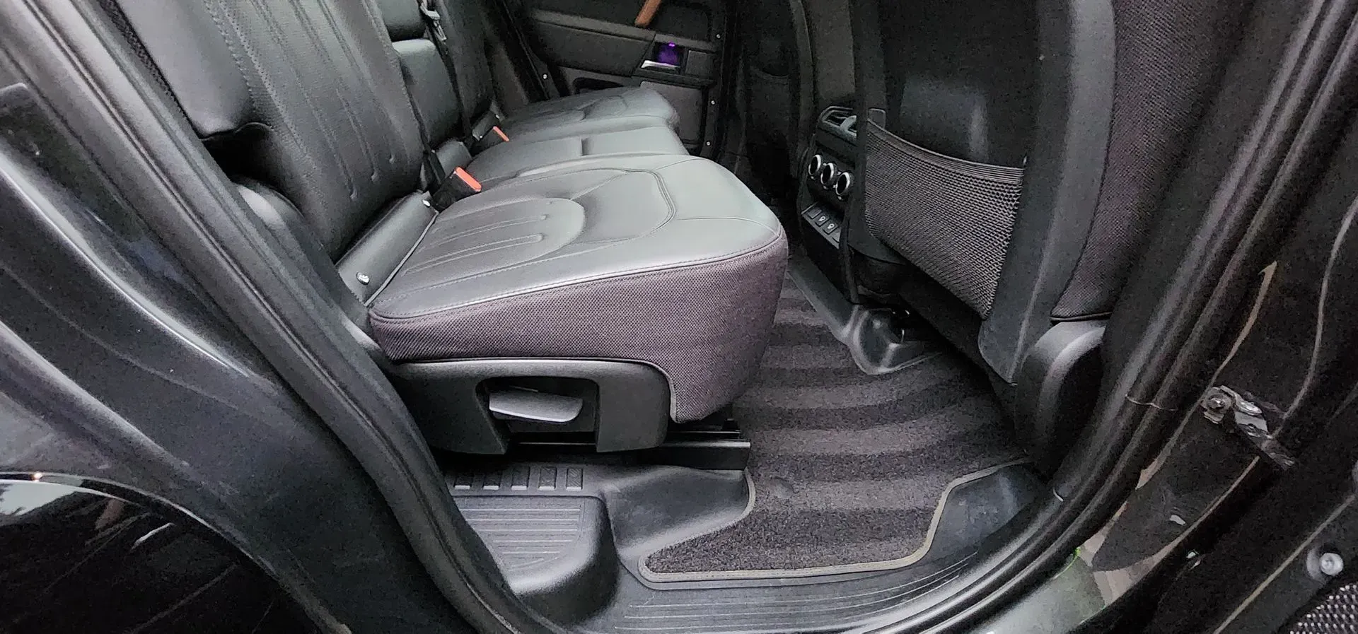Car rear interior with folded seat and dark floor mats in a black vehicle interior