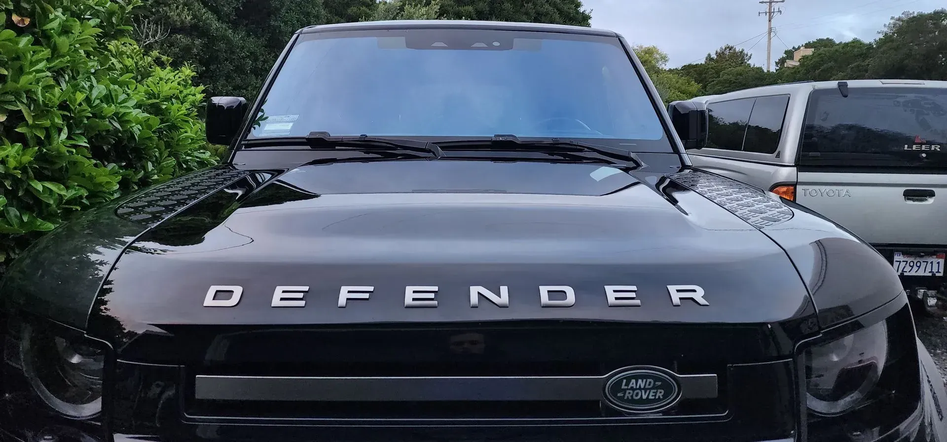 Black Land Rover Defender front view in a parking lot, with bold DEFENDER lettering on the hood