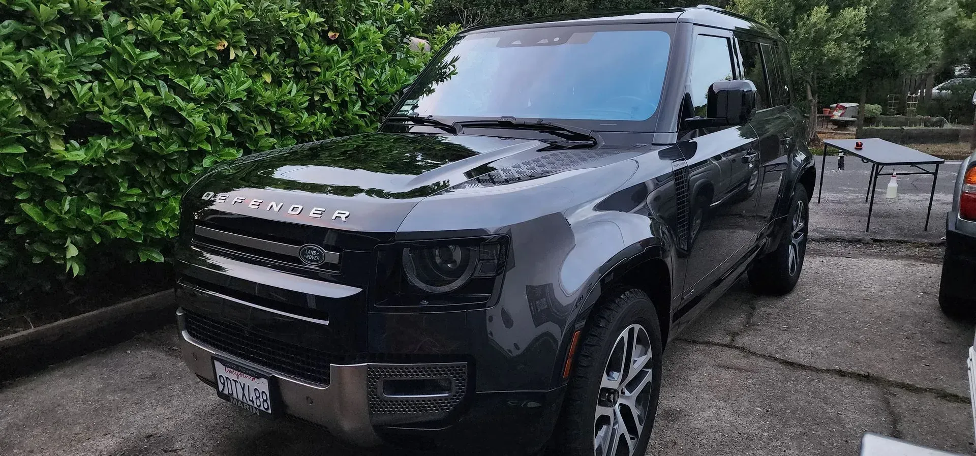 Black Land Rover SUV parked on a wet driveway beside a hedge