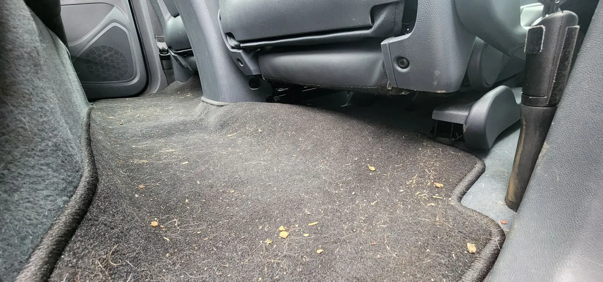 Car interior with a dirty, crumb-covered floor mat on the back seat floor