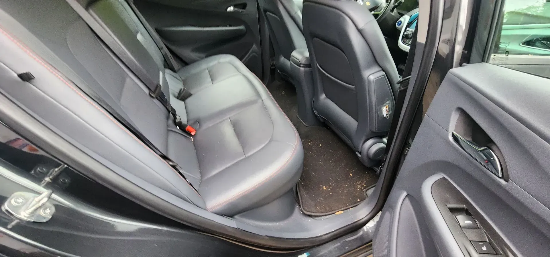 Back seat interior of a black car with gray leather seats and open rear door