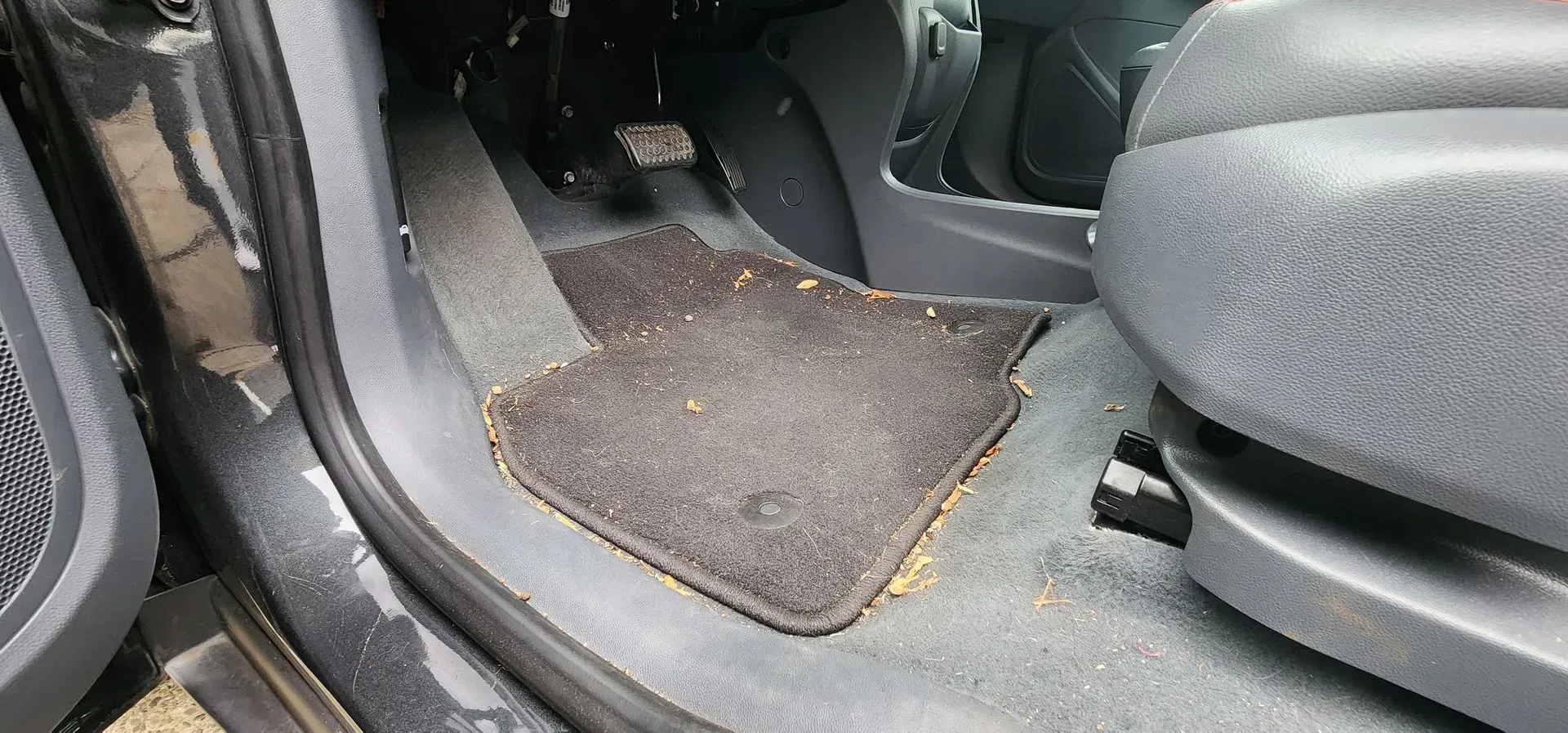 Car interior footwell with black floor mat and seat base visible