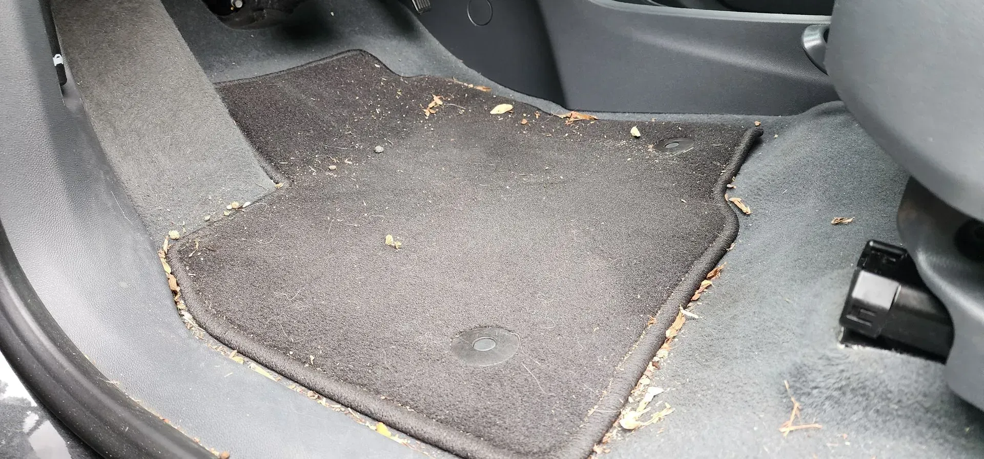 Car floor with black mats and scattered dirt near the rear seat area.
