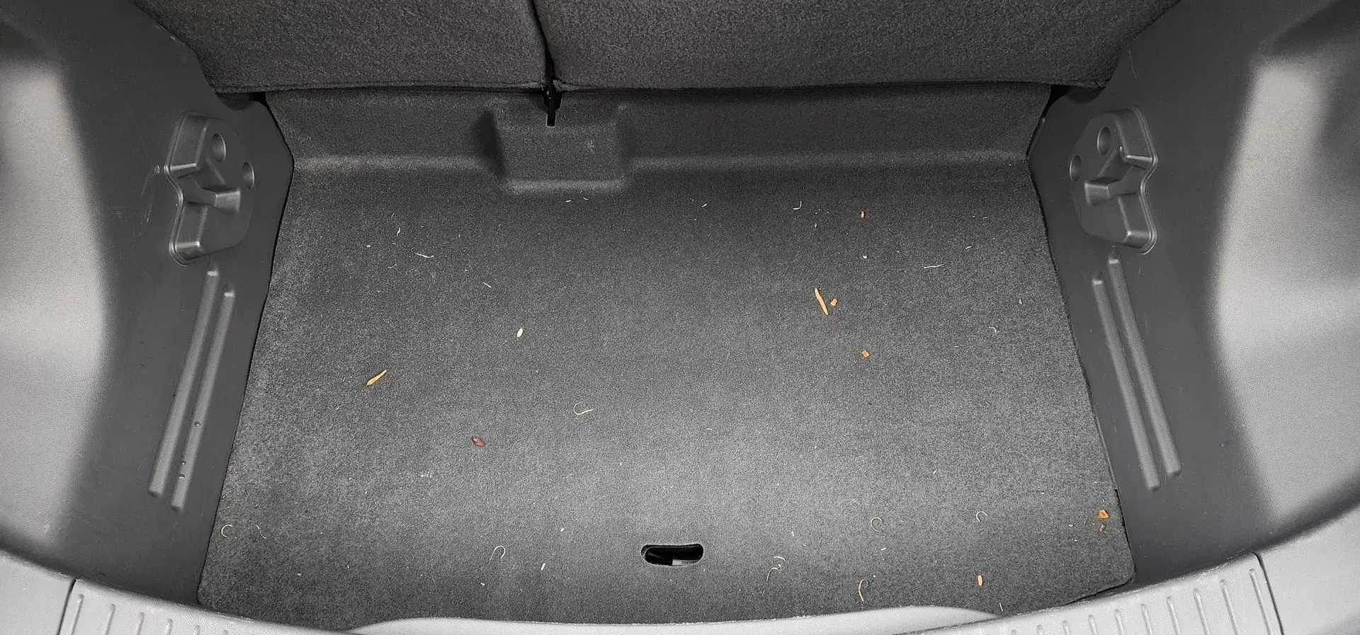 Empty car trunk with gray carpeted interior and a small latch opening near the back
