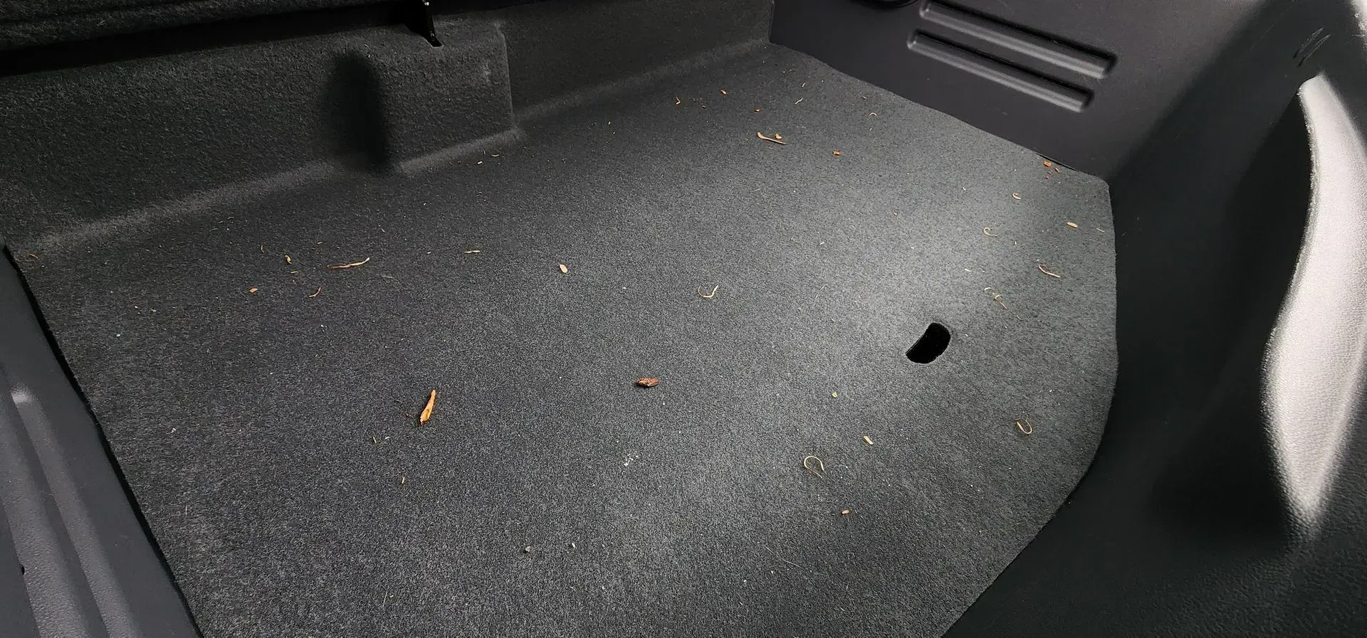 Car trunk interior with black carpeted floor and side panels, showing a small hole on the right side.