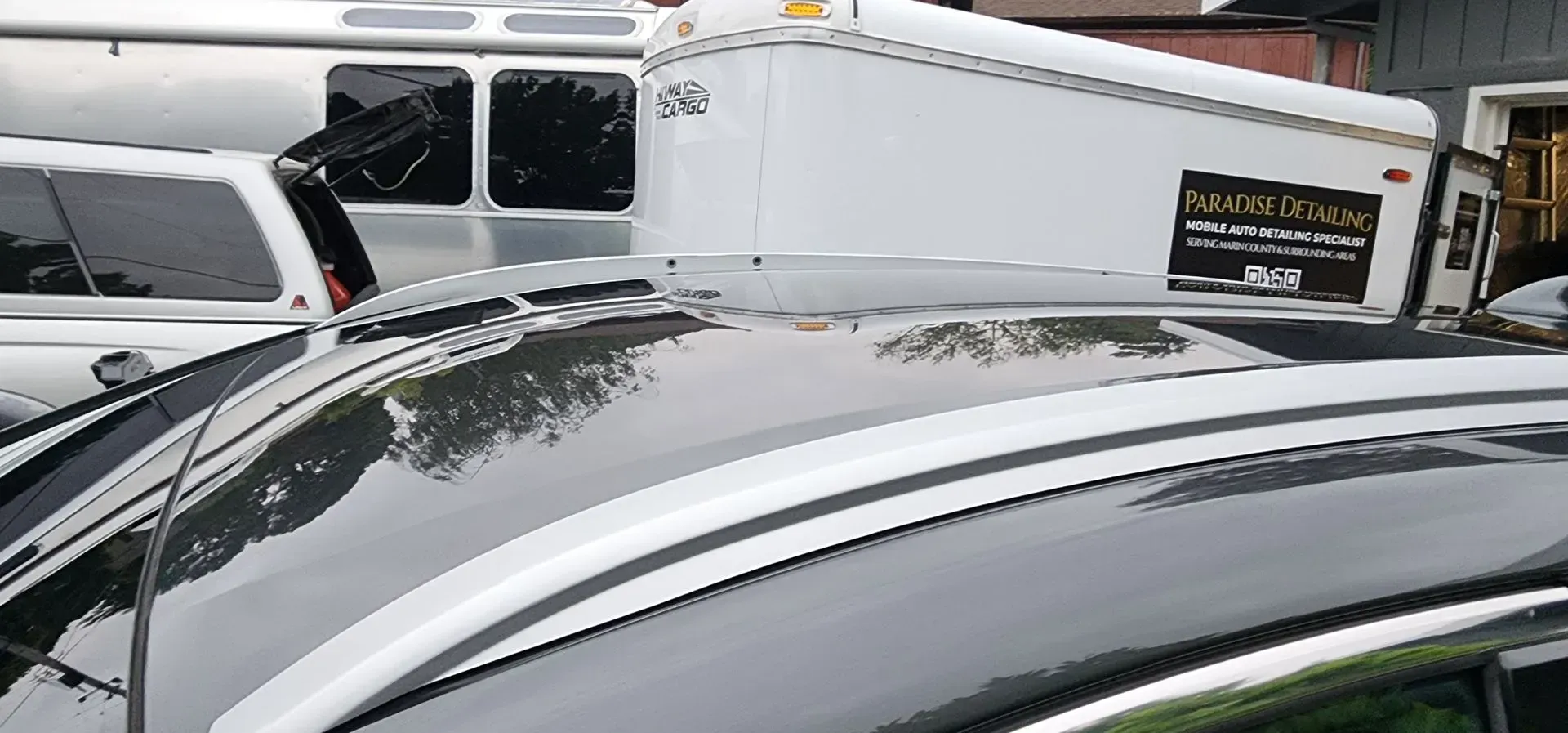 Snow-covered car roof in front of parked vans and a white trailer with a logo sign