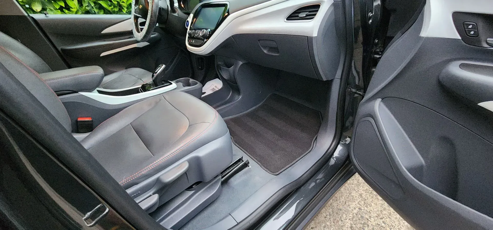 Car interior with open door, showing black leather front seats and dashboard from the passenger side.