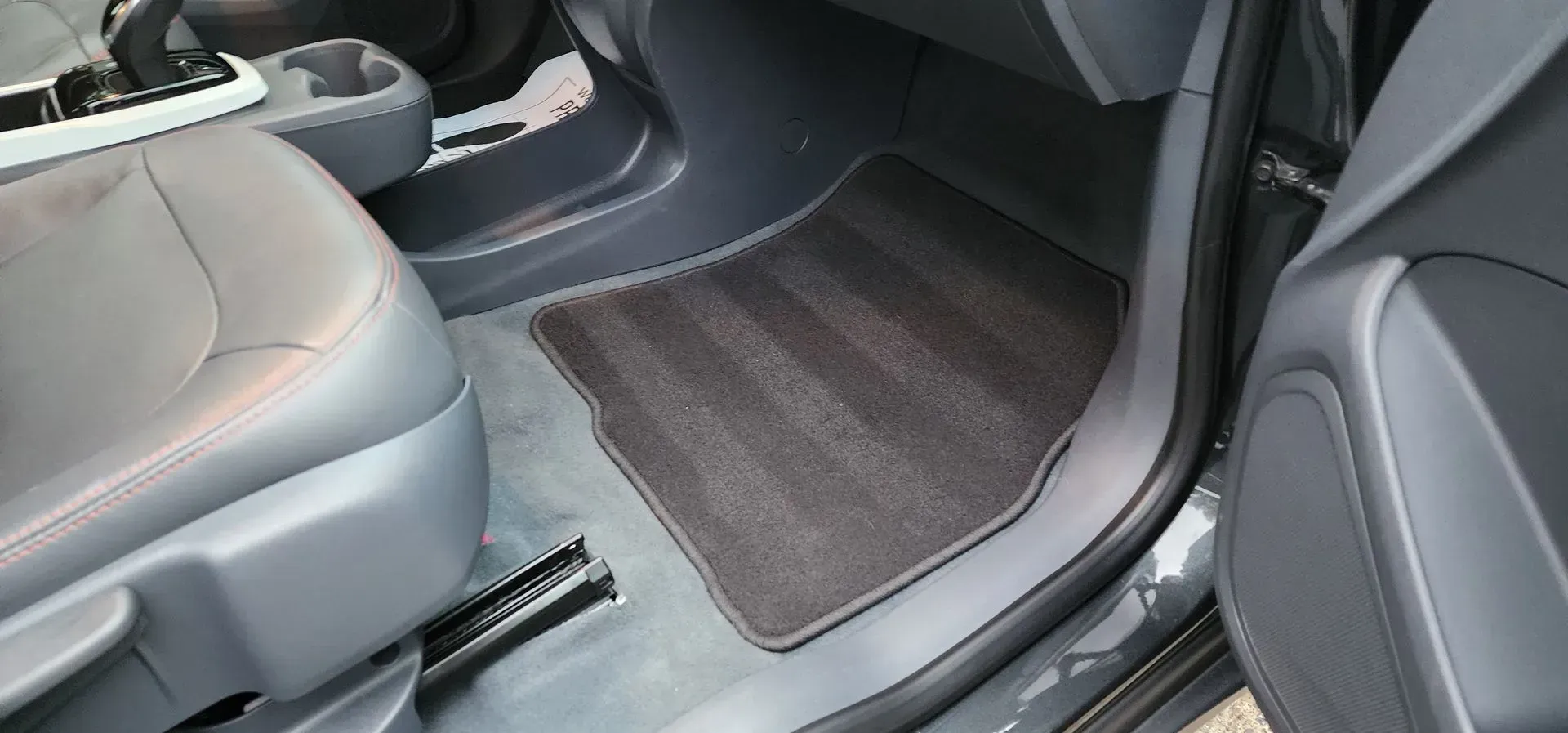 Car interior with gray seats and a dark floor mat in the back footwell
