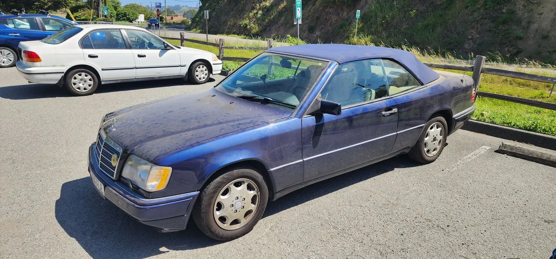 Blue two-door coupe parked in a lot on a sunny day, with another car behind it.
