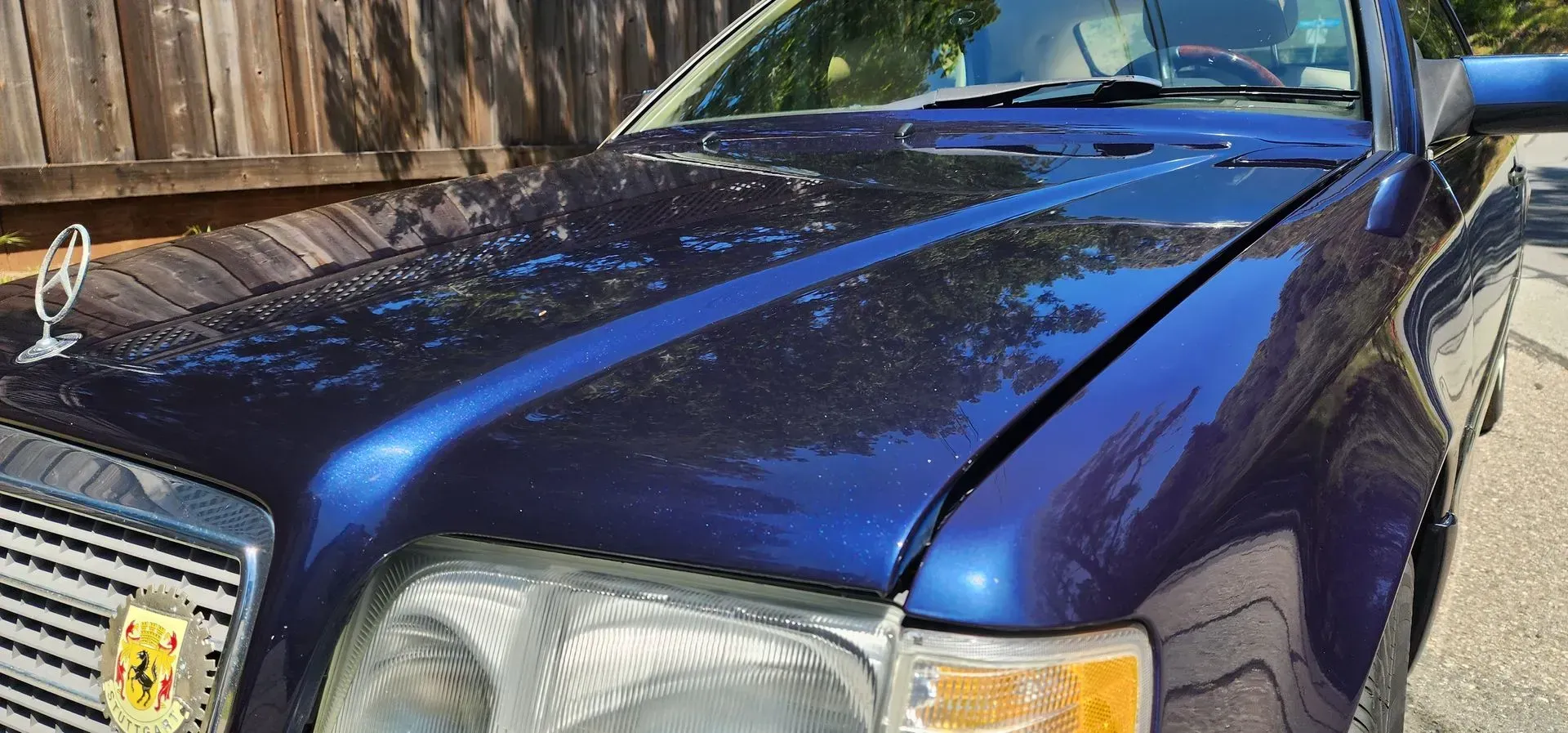 Blue Mercedes-Benz car parked outdoors beside a wooden fence