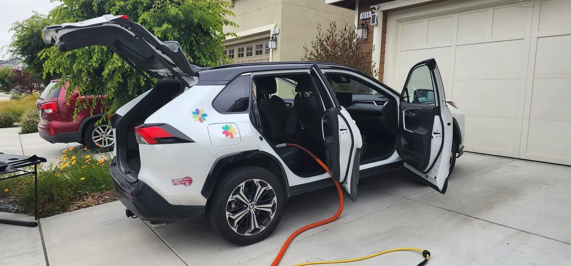 White SUV parked in a driveway with both side doors open and a charging cable connected to the rear side