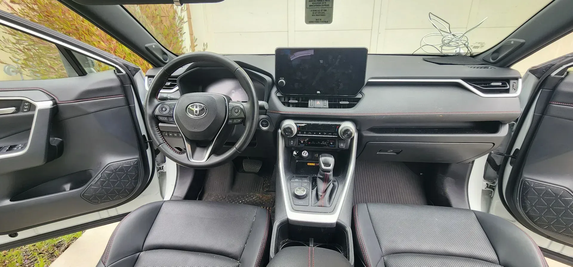 Car interior with black dashboard, steering wheel, center console, and front seats; driver and passenger doors open.