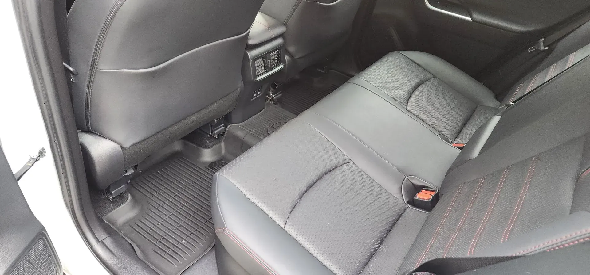 Rear car seat with black leather upholstery and floor mats, viewed from the open door