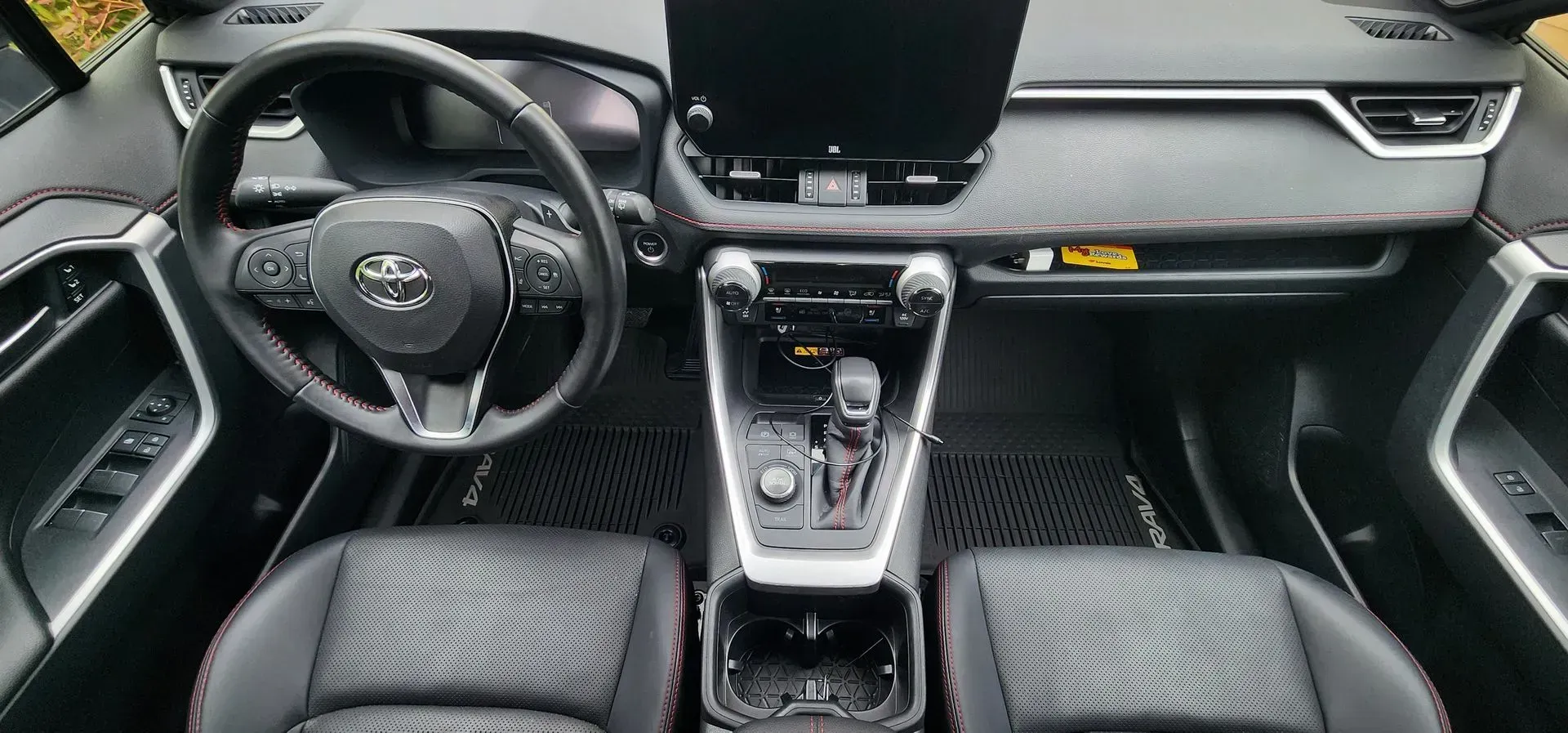 Modern car interior with black steering wheel, center console, digital display, and quilted seats