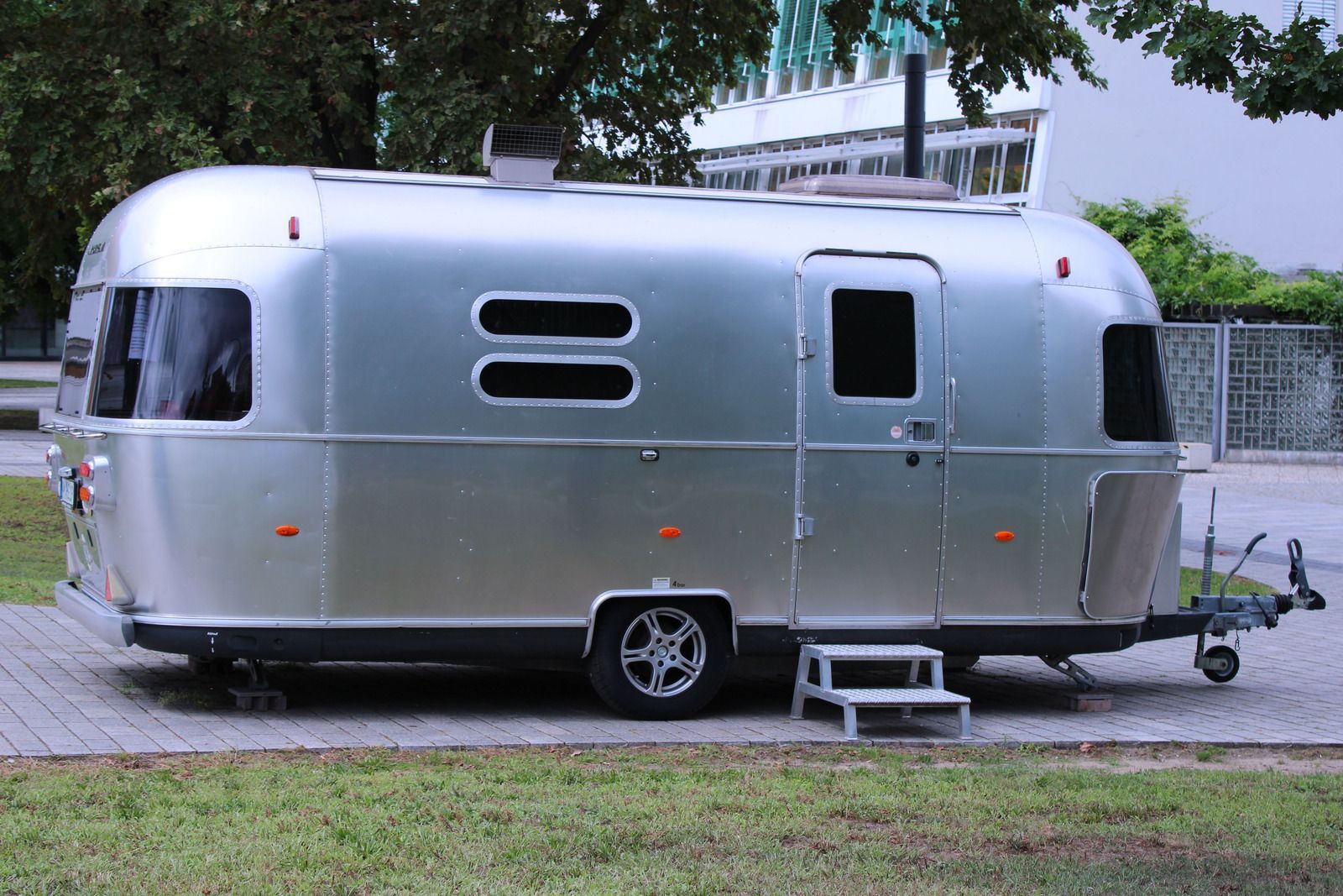 Silver Airstream-style travel trailer parked on a paved driveway beside grass and trees