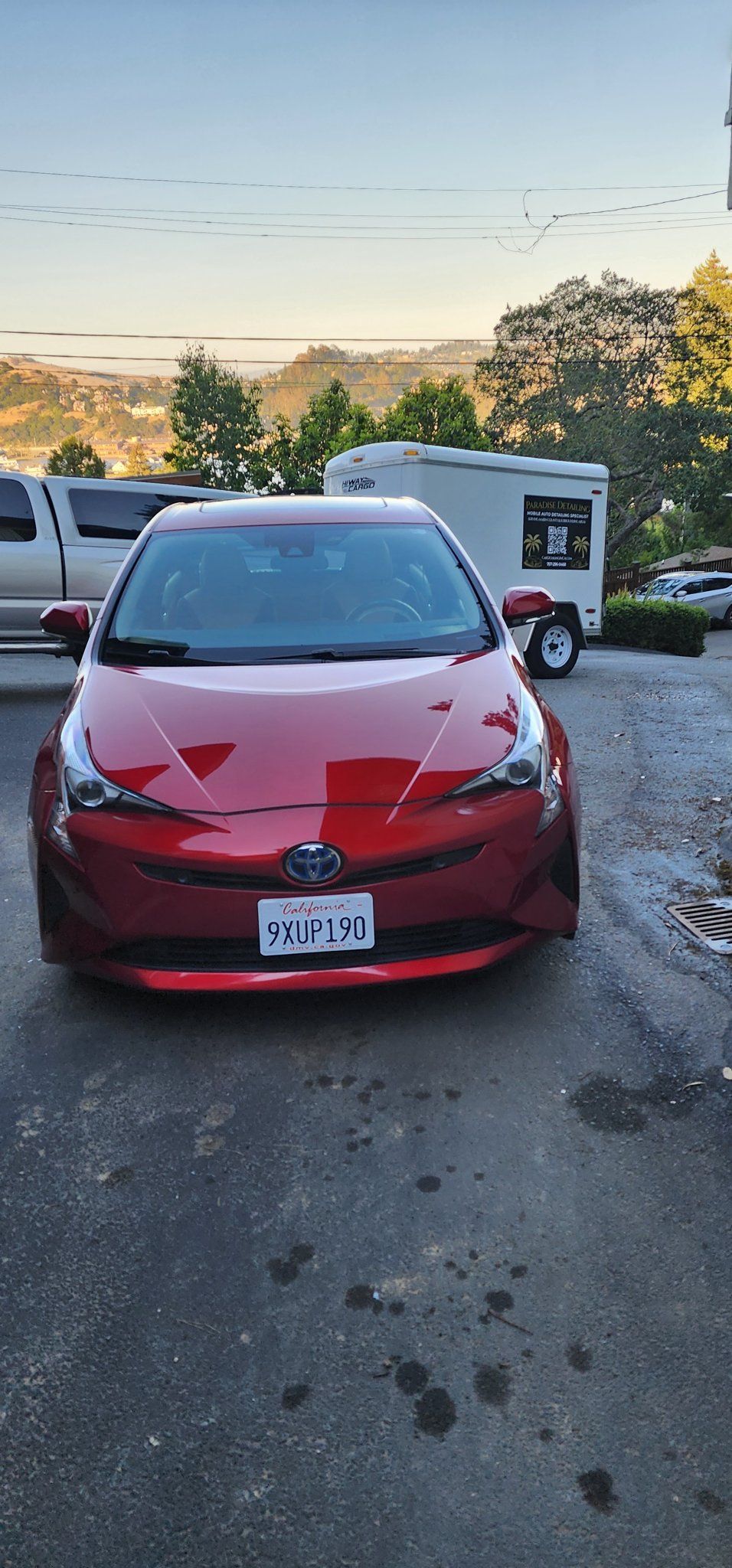 Red compact car parked in a lot at dusk, front view with a damaged hood.