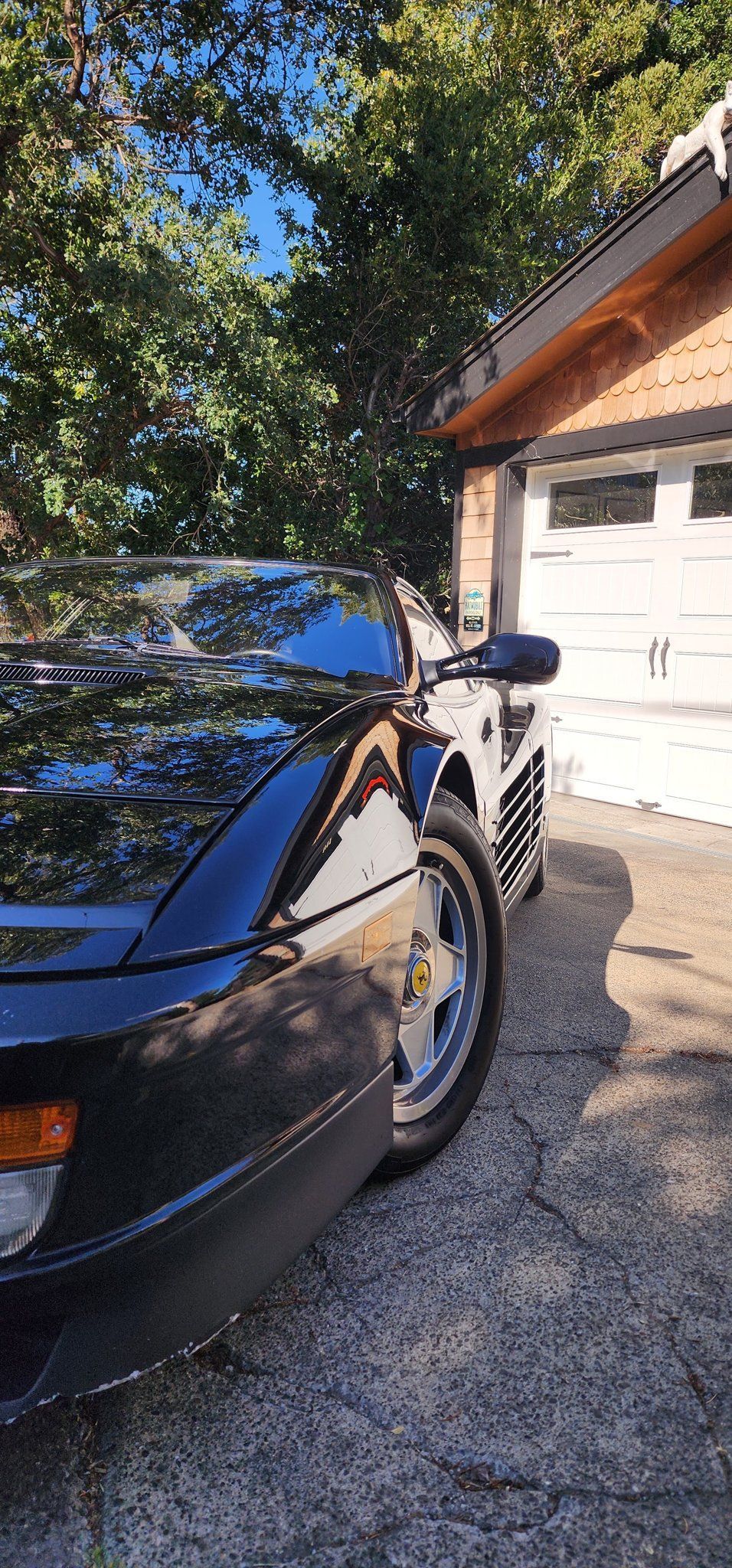 Blue car parked on a gravel driveway beside a white garage in sunlight
