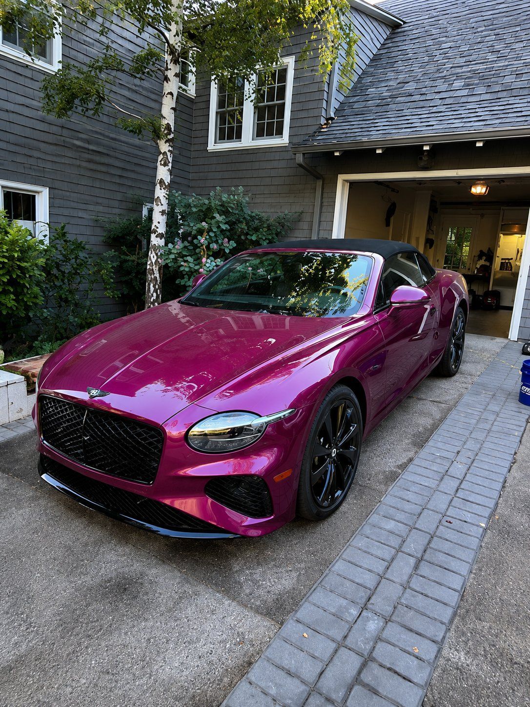Magenta sports coupe parked in a driveway beside a house and garage.
