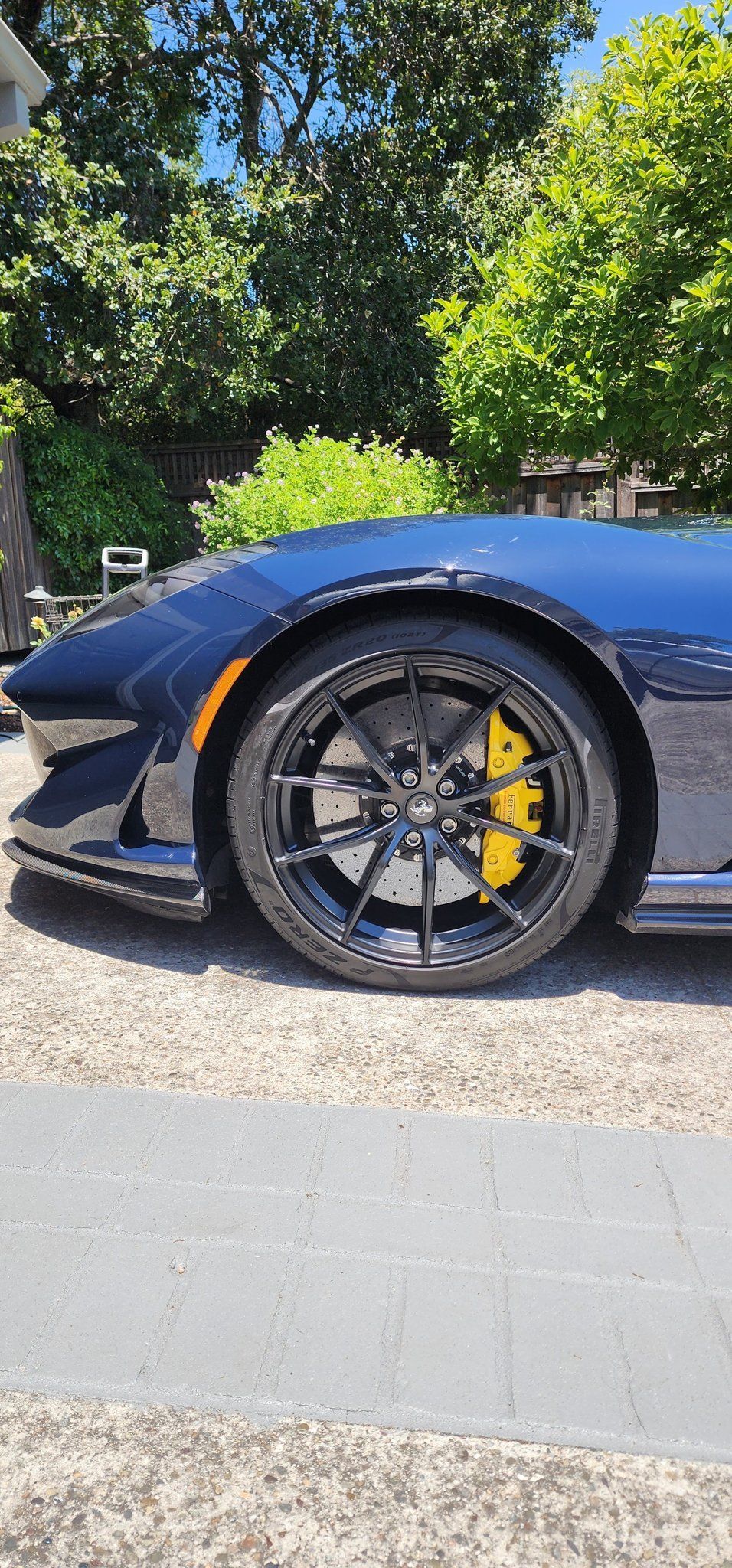 Blue sports car front wheel and side panel on a sunny roadside, with yellow brake calipers.