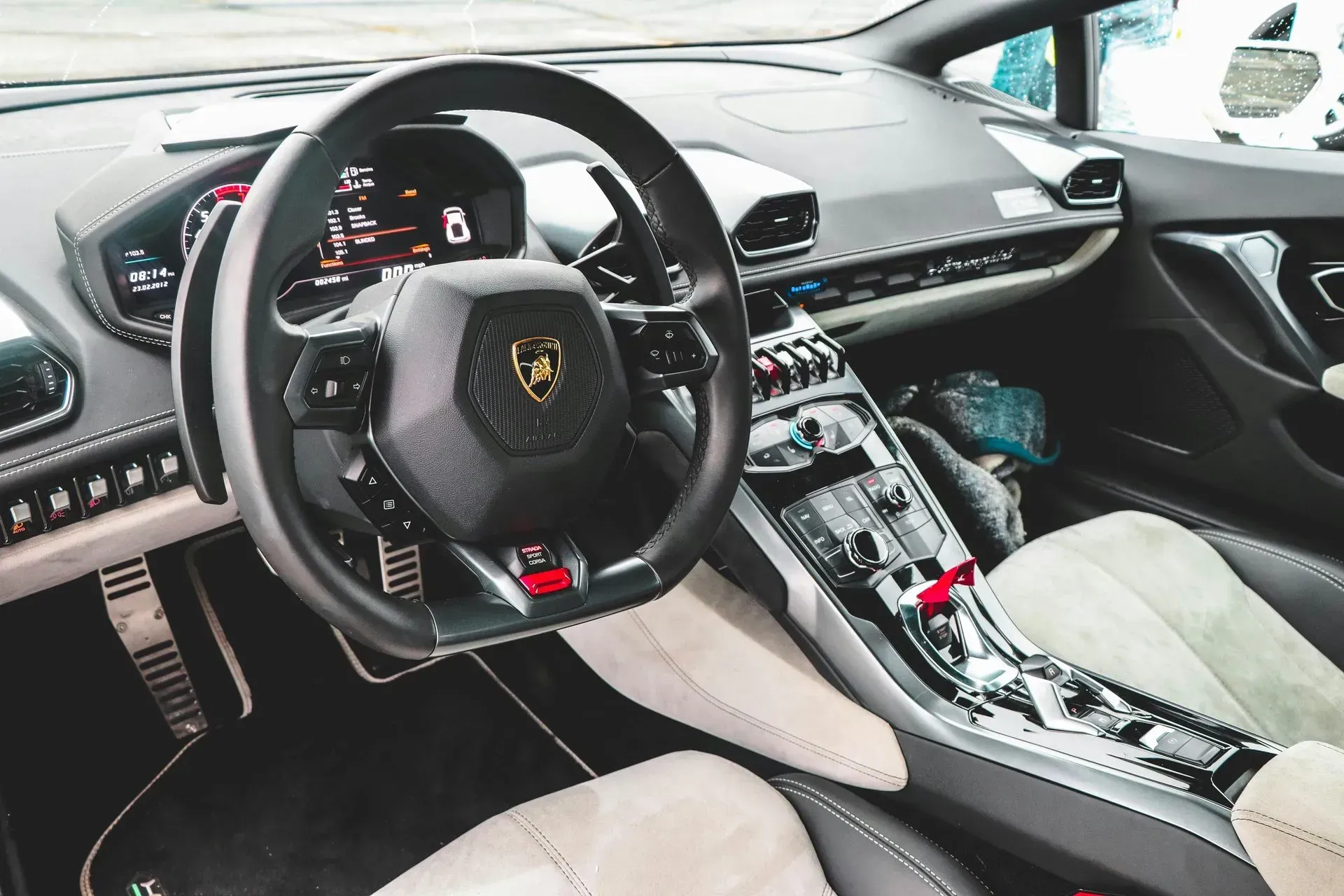 Luxury sports car interior with black steering wheel, beige seats, and silver center console.