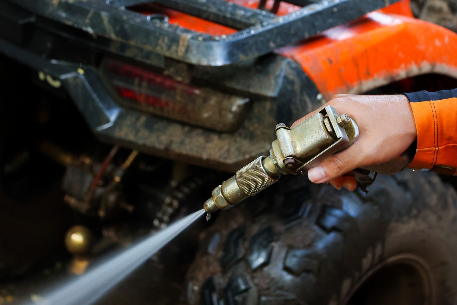Hand spraying water on a muddy ATV tire and front grill with a pressure washer.