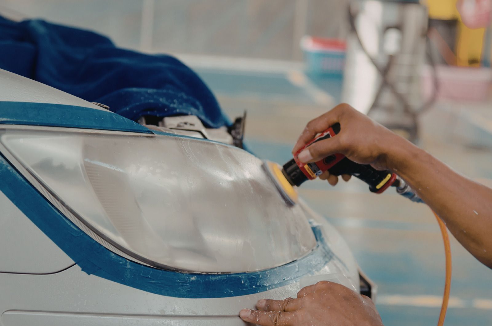 Hand sanding the clear lens of a blue vehicle or boat with a power sander