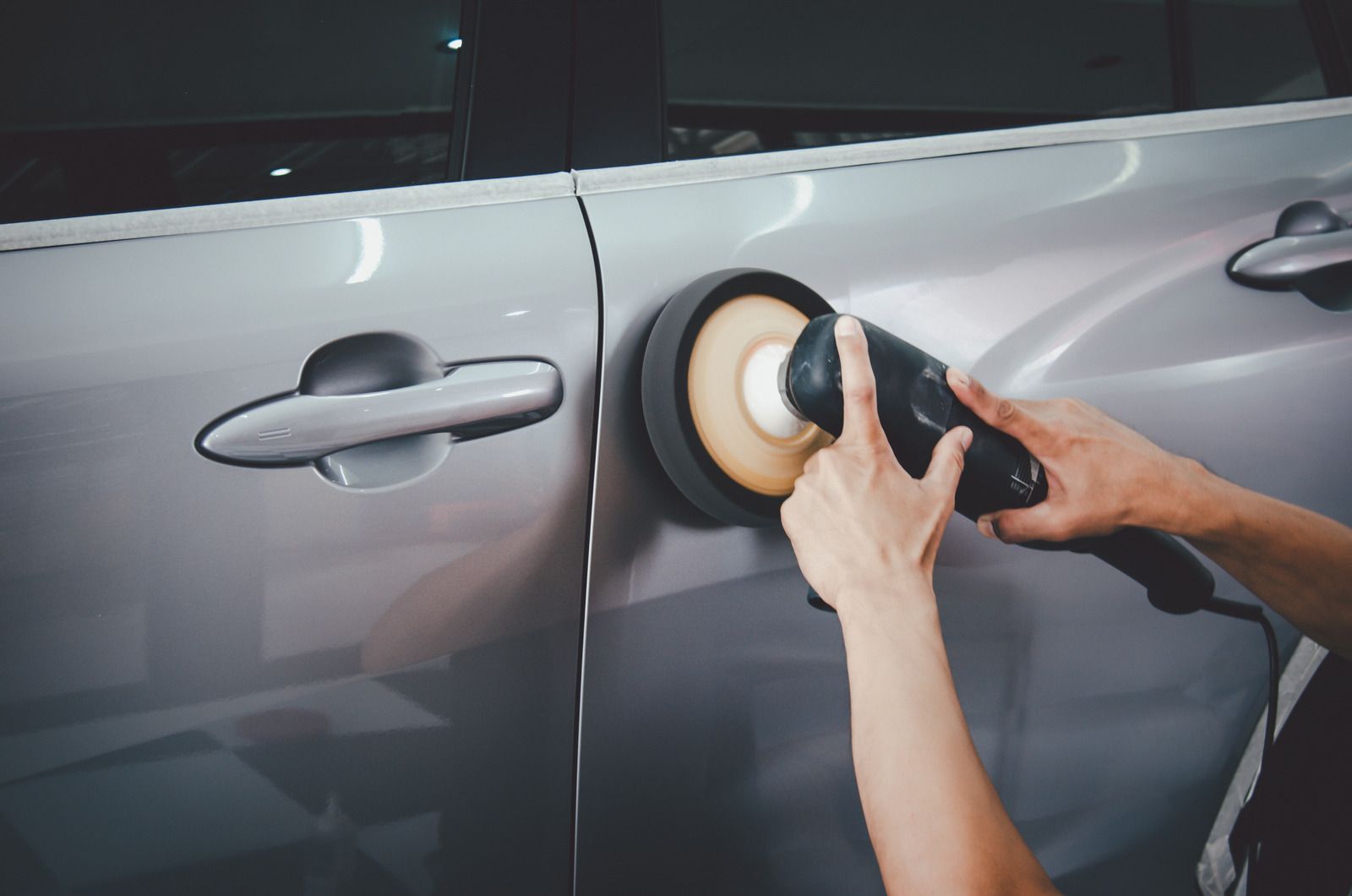 Hands polishing a gray car door with a buffer tool