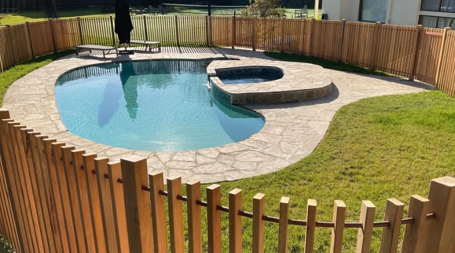 Wooden pool safety fence surrounding a backyard swimming pool