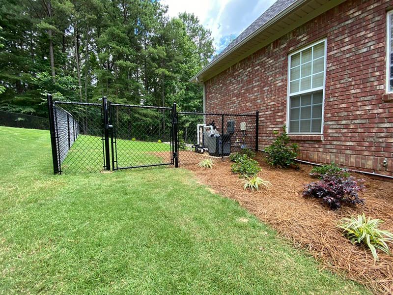 Backyard with black chain-link fence, brick house, and a small landscaped garden bed.