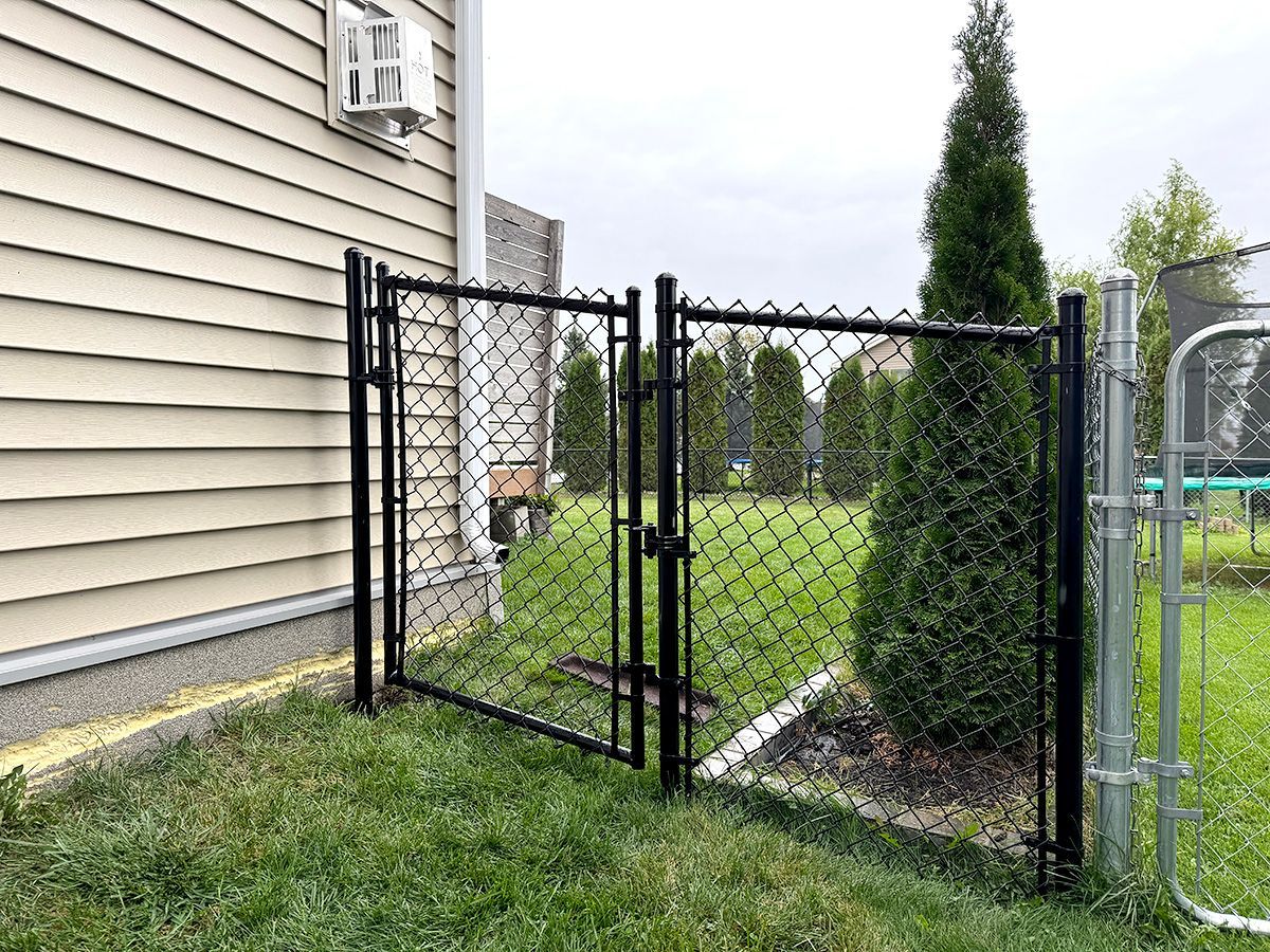 A black chain-link double gate installed in a backyard next to the light-colored siding of a house.