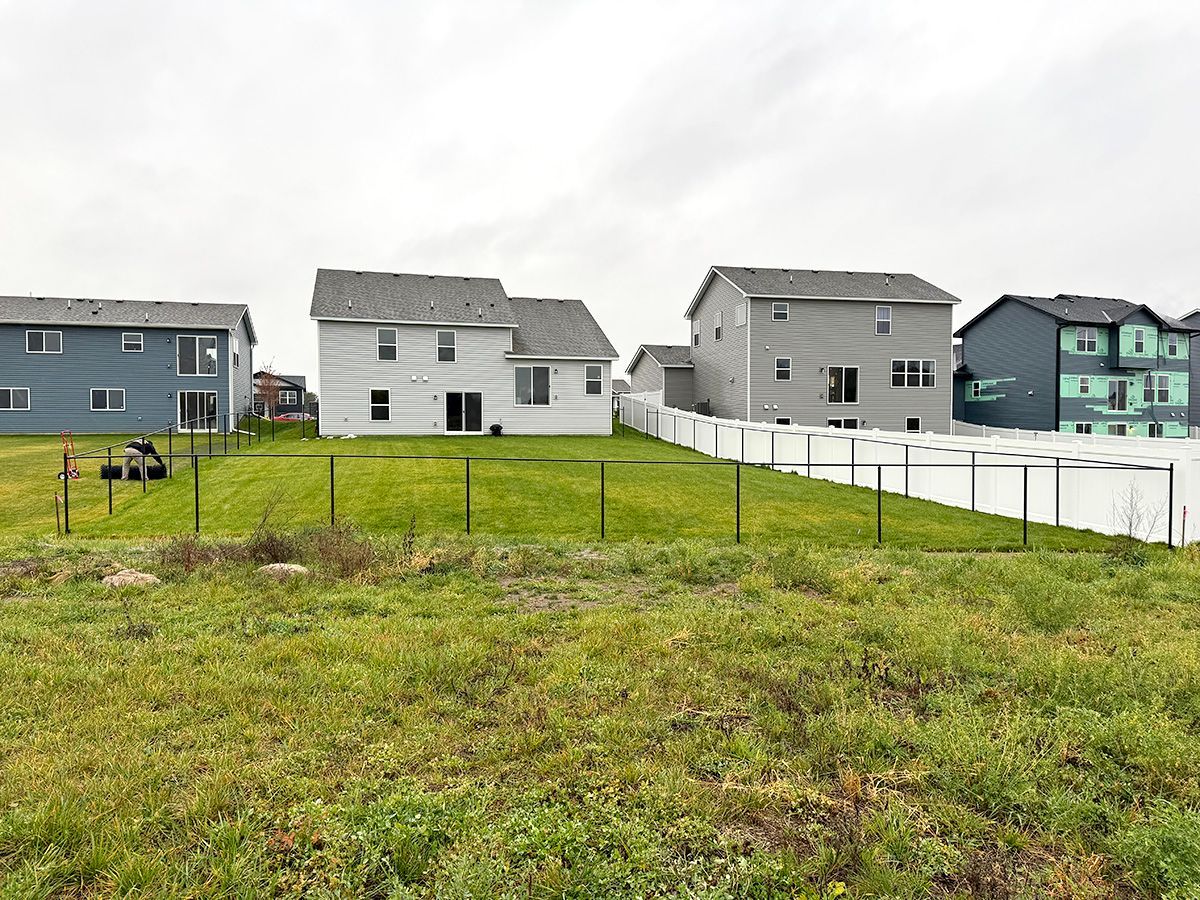 A view of residential houses with backyards, separated by chain-link and white privacy fences, under a cloudy sky.