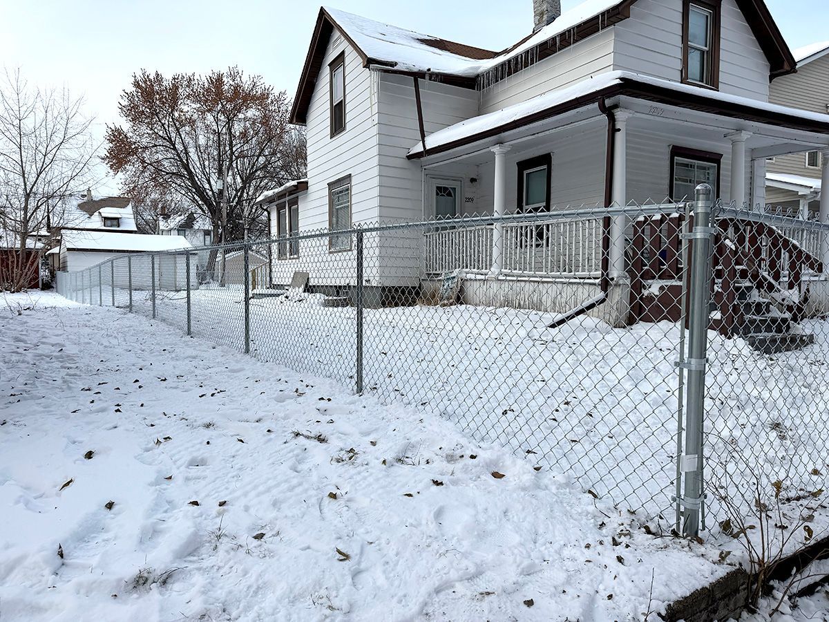 Snow-covered house and yard with chain-link fence on a winter day