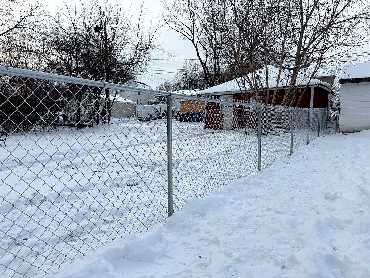 A metal chain-link fence runs through a snow-covered yard, with a small garage visible in the background.
