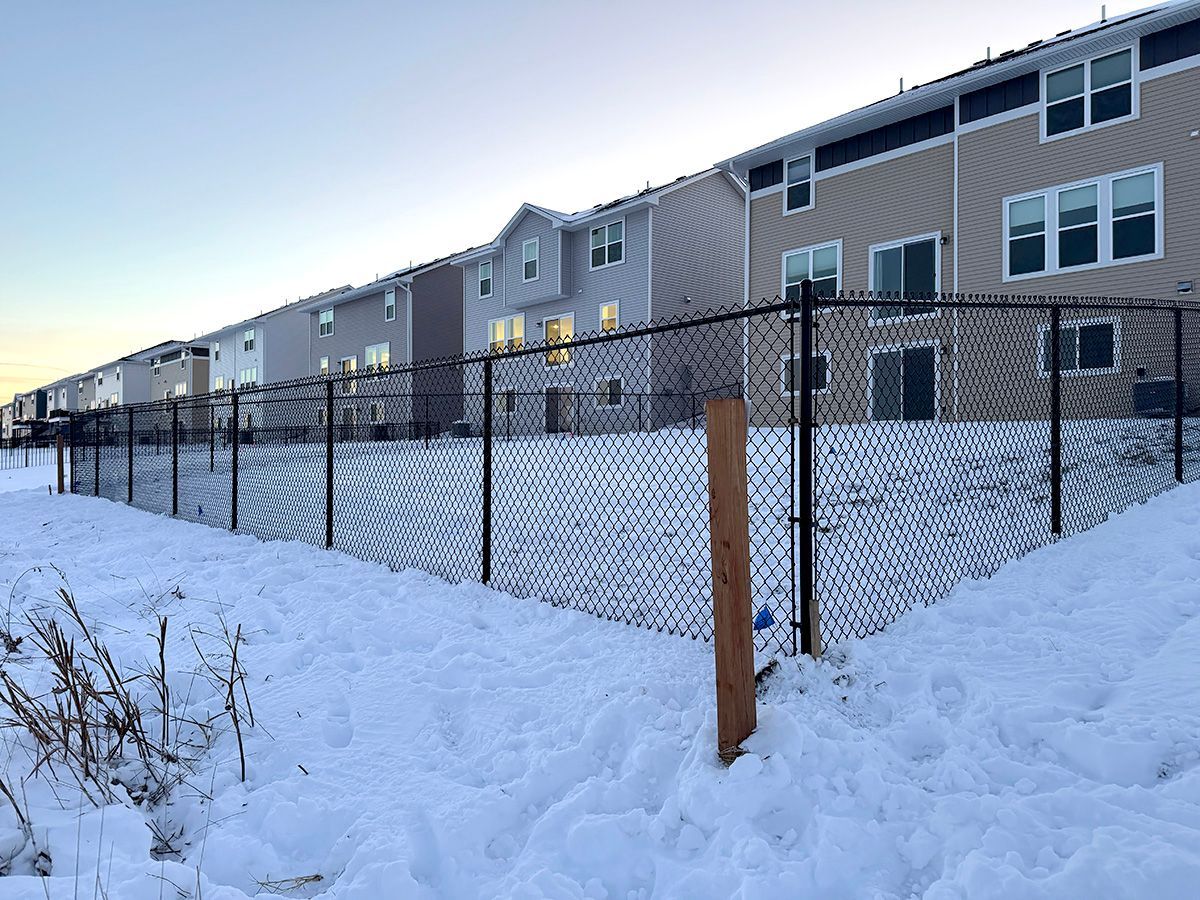 A row of multi-story townhouses seen behind a black chain-link fence on a snowy, overcast day.