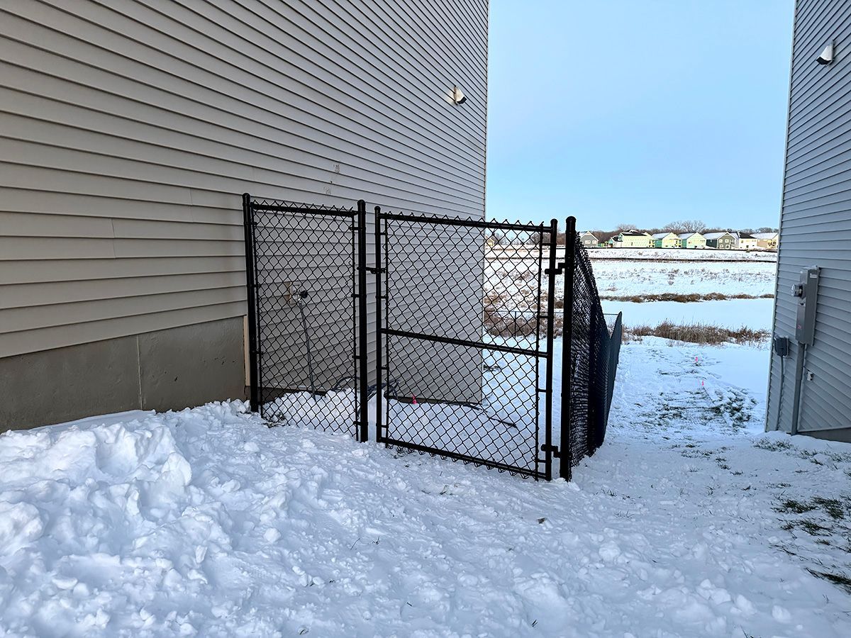 A black chain-link gate sits between two houses in a snowy residential area.