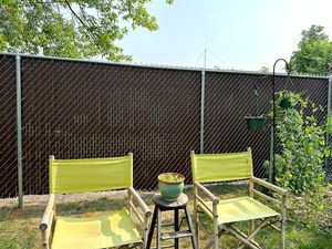 Two yellow folding chairs sit on grass in front of a brown chain-link fence, with a small potted plant on a stool between.