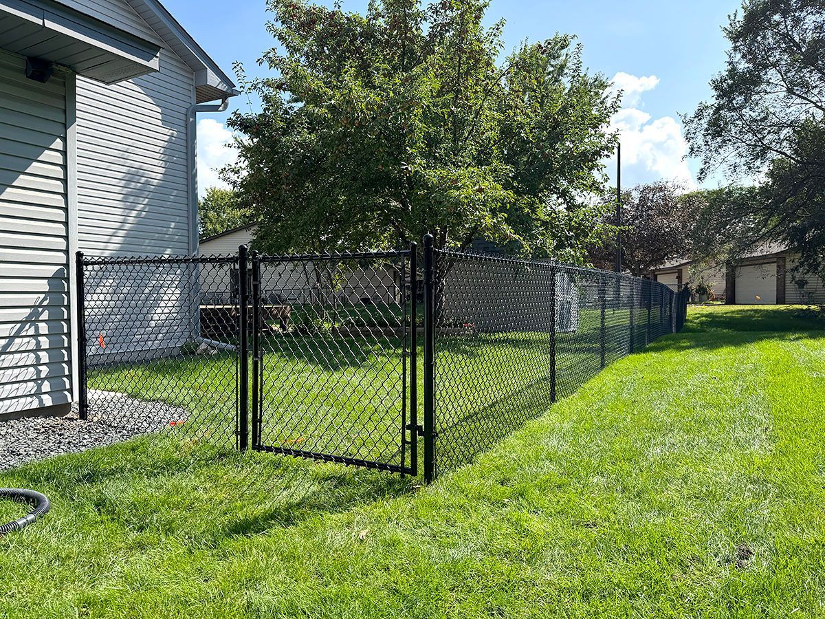 Black chain-link fence with a closed gate installed in a residential backyard next to a house.