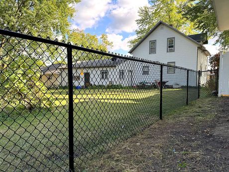 A black chain-link fence runs diagonally across the foreground, framing a residential backyard with a white house.