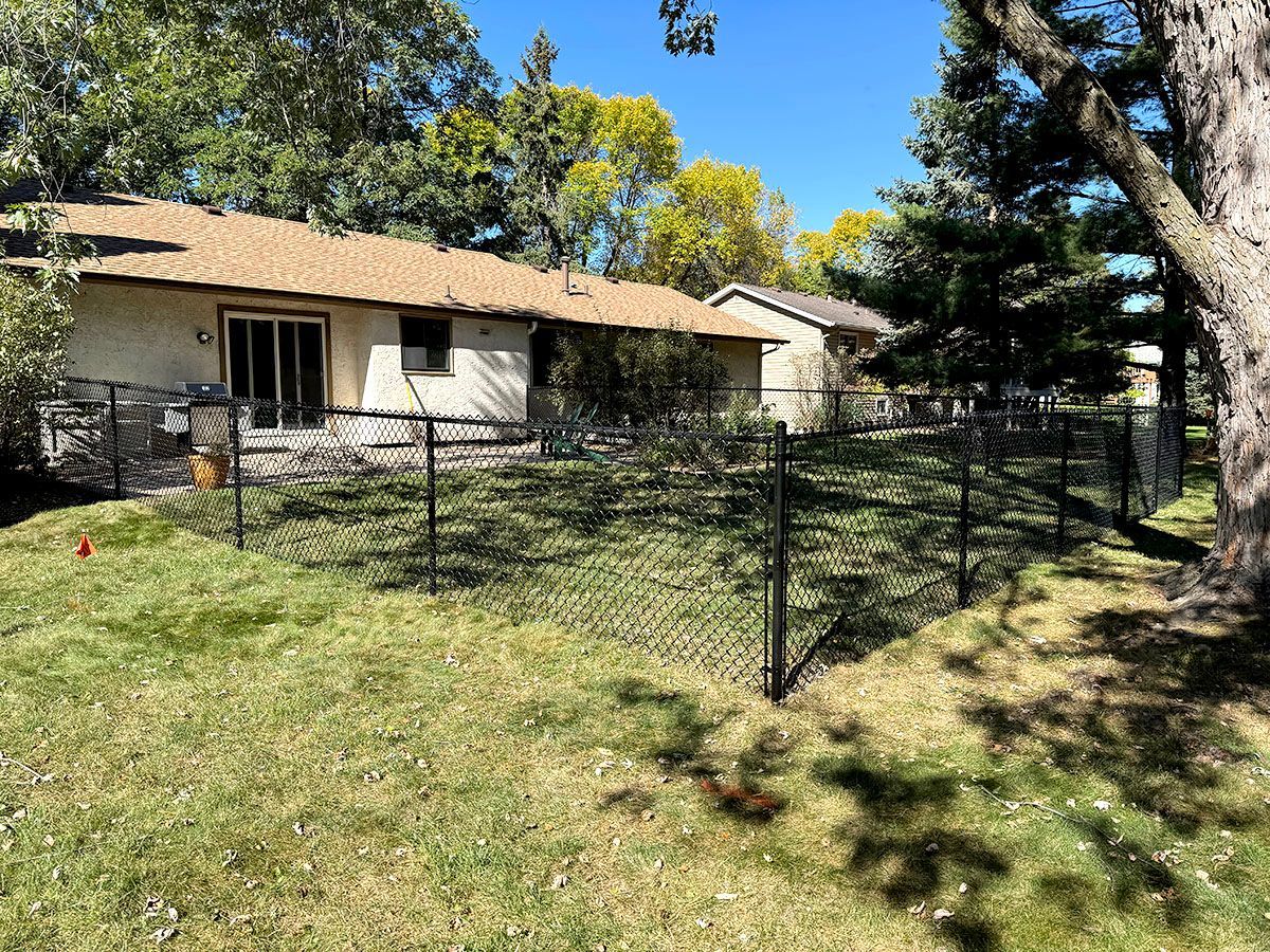A tan house with a fenced-in backyard and a lawn on a sunny day with trees in the background.