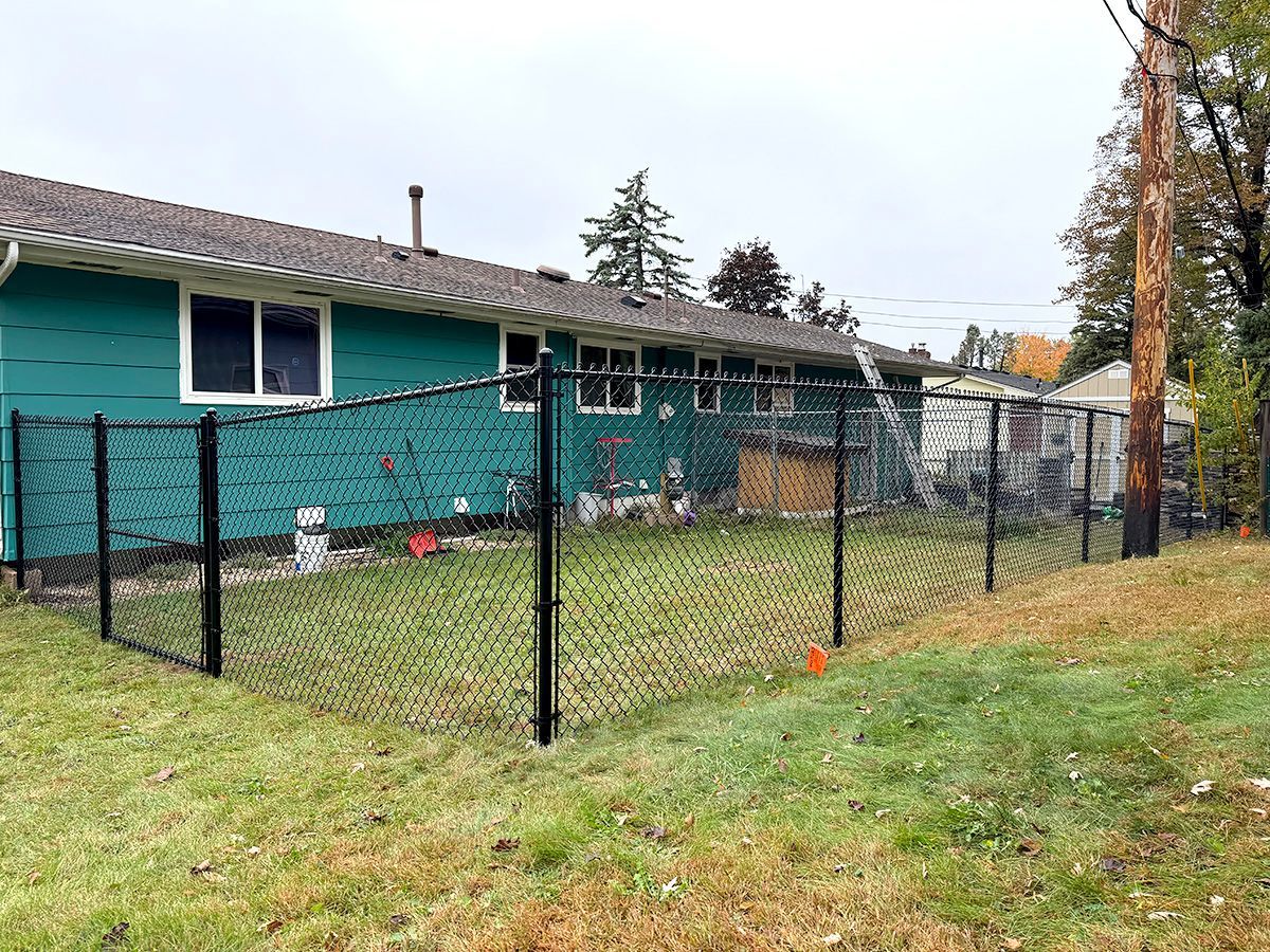 A teal house with a black chain-link fence enclosing a backyard in a grassy residential area.