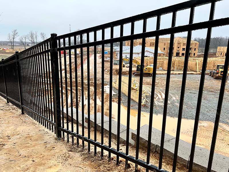 Black metal fence along a dirt path overlooking a construction site and excavated ground