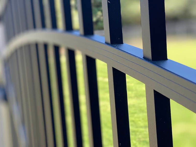 Close-up of a white metal railing with blue posts against a blurred green background