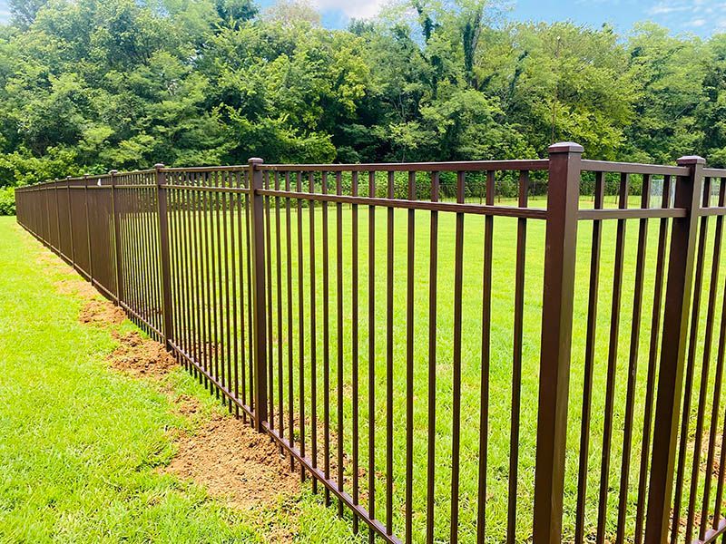 Brown metal fence lining a bright green lawn beside dense trees
