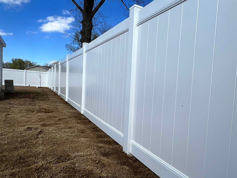 White vinyl privacy fence along a dirt yard under a blue sky