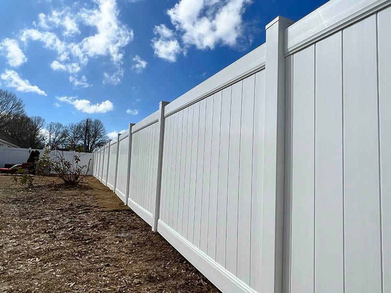 White vinyl privacy fence along a dirt yard under a blue sky with clouds