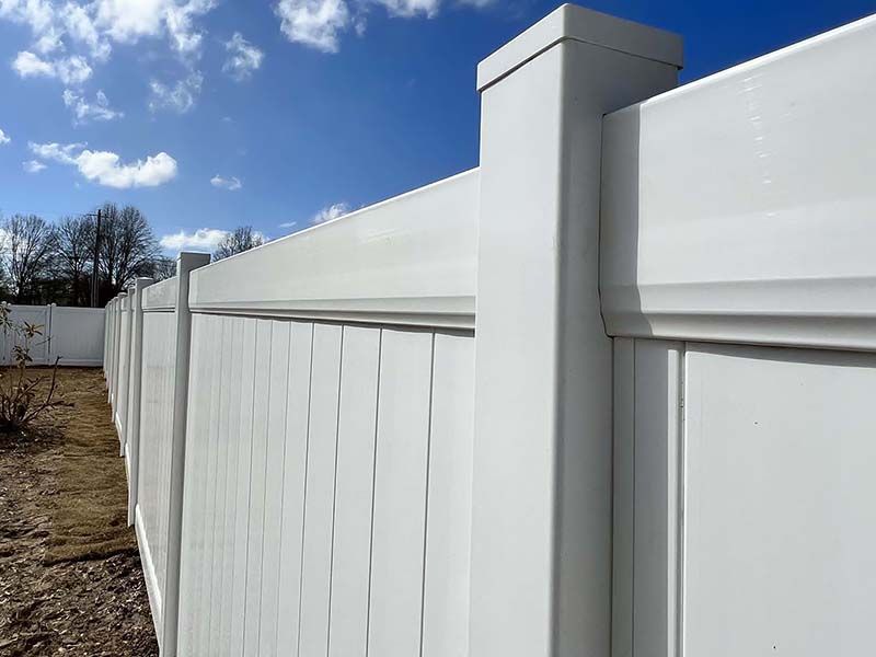 White vinyl fence with a gate and post beside a gravel yard under a blue sky.